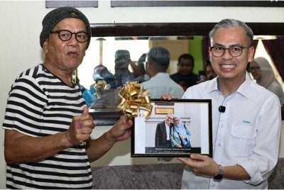 Fahmi (kanan) menerima cenderahati daripada Ahmad selepas menyampaikan sumbangan Tabung Kasih@Hawana di kediamannya di Kampung Lubuk Batu pada Ahad. Foto: Bernama 