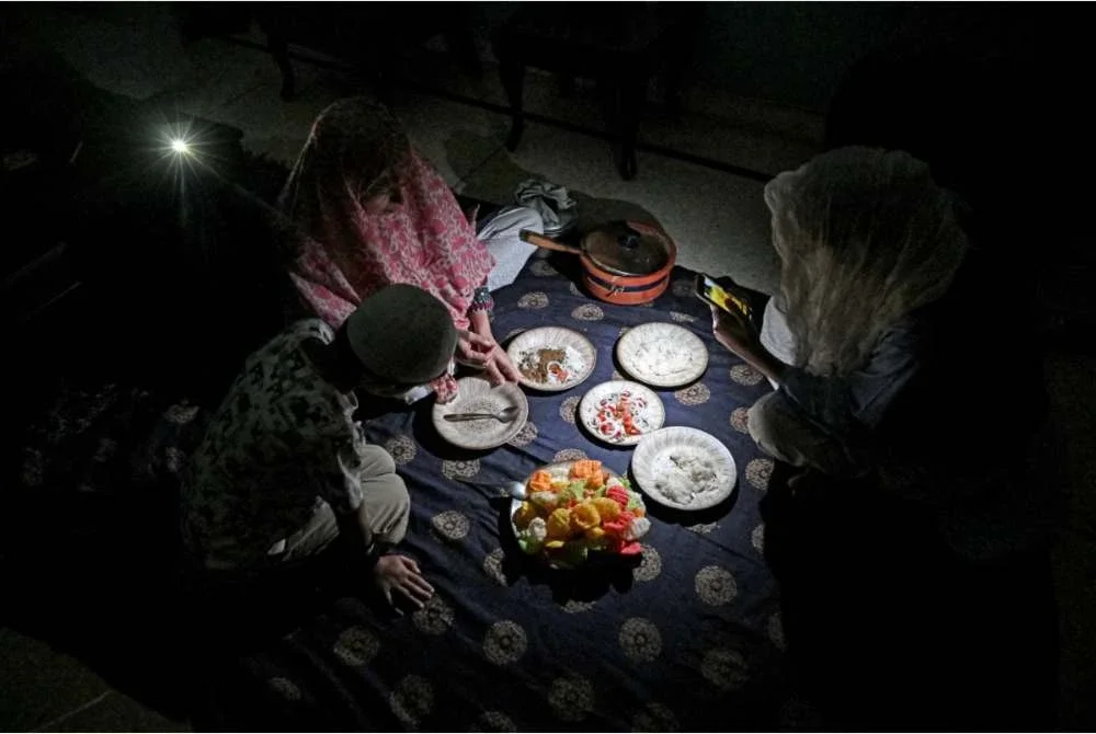 Sebuah keluarga di Islamabad terpaksa menikmati makan malam dengan diterangi cahaya lampu telefon bimbit. - Foto Agensi