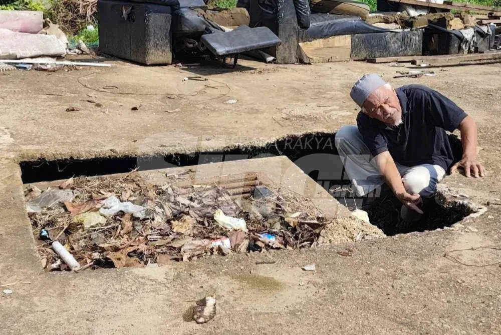 Mazlan menunjukkan lubang akibat mendapan tanah yang didakwa berpunca daripada sistem saliran lama.