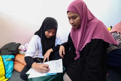 Nurmazehra (kiri) dibantu kakaknya, Norhana mengisi borang permohonan bantuan persekolahan ketika ditemui di Pusat Pemindahan Mangsa Kebakaran di Dewan Sekolah Kebangsaan Kampung Gas. Foto Bernama
