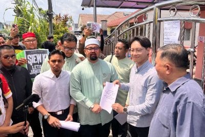 Mohamed Sukri (tengah) menyerahkan memorandum bantahan dan tuntutan permohonan maaf kepada wakil ADUN Seri Kembangan, Tey Boon Kiat di Serdang pada Jumaat
