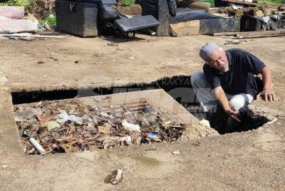 Mazlan menunjukkan lubang akibat mendapan tanah yang didakwa berpunca daripada sistem saliran lama. 