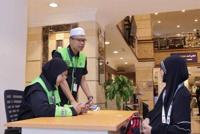 Azrisham memberikan bantuan kepada salah seorang jemaah yang memerlukan khidmat mereka. - FOTO: TH