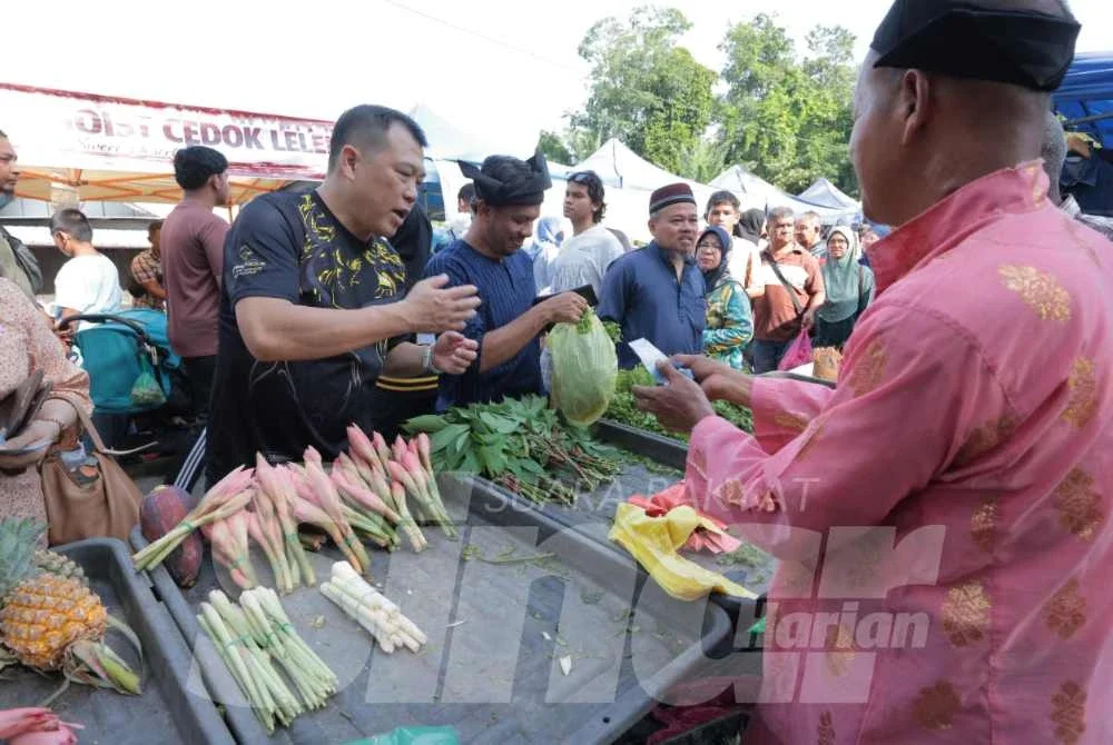 Sze Yee (kiri) bersama Nor Akmal menyantuni para peniaga sempena Program Santai Media@Pasar Pagi Sungai Bayor pada Jumaat.