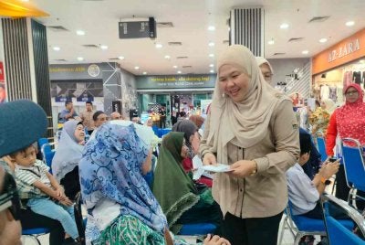 Salbiah (berdiri) menyerahkan Kad Perak Sejahtera kepada penerima selepas menyempurnakan Majlis Penyerahan Kad Perak Sejahtera di Pasar raya Mydin pada Isnin.