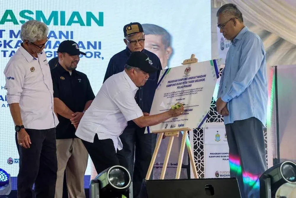 Mohamad (tengah) menandatangani plak perasmian Kampung dan Sekolah Angkat Madani di Kampung Guar Petai di Tasek Gelugor pada Jumaat. - FOTO: Bernama
