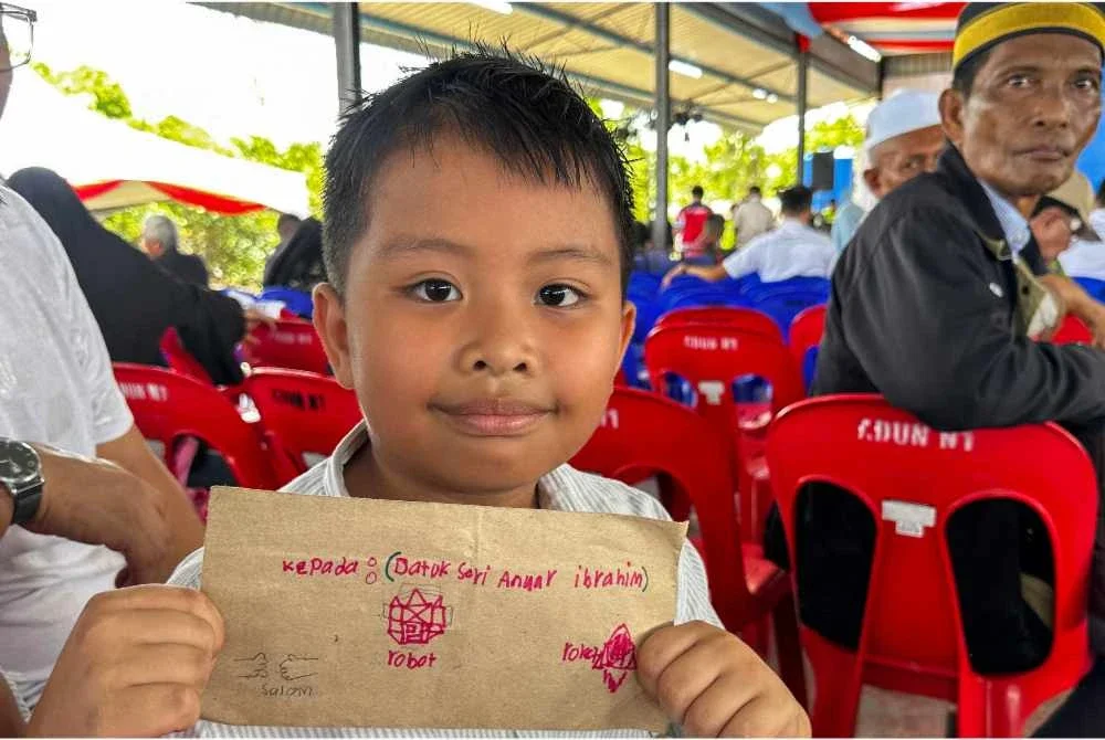 Seorang kanak-kanak, Syam Aariz Rayyan Abdullah,8, menyerahkan sepucuk surat kepada Perdana Menteri Datuk Seri Anwar Ibrahim pada program Perdana Menteri bertemu penduduk di Pekan Baru Pulau Banggi hari ini. Foto Bernama