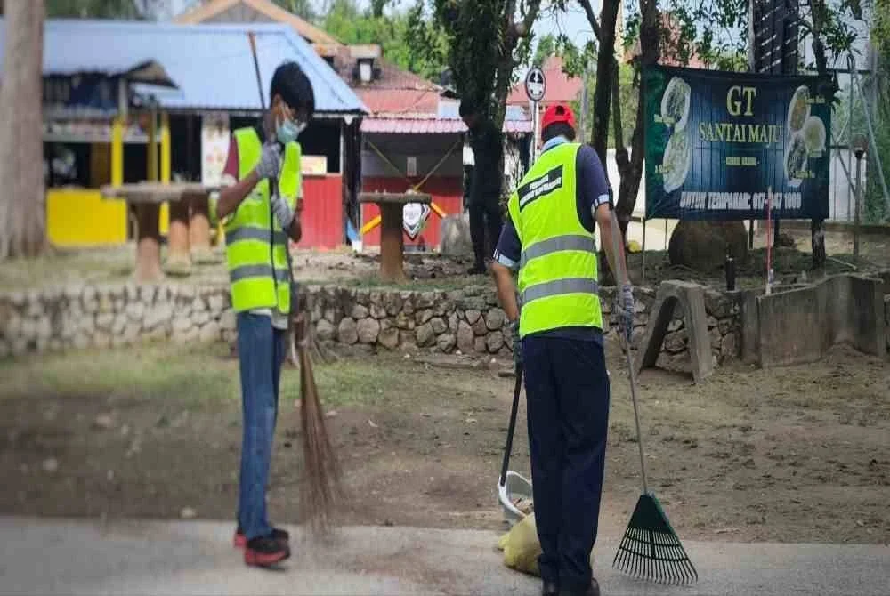 Muhammad Adli bersama seorang lagi lelaki sedang melakukan kerja pembersihan di Taman Gelora pada Ahad.
