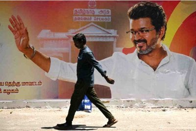 Seorang lelaki berjalan melepasi poster kemenangan Vijay dalam pilihan raya negeri, di Chennai. Foto AFP