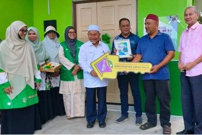 Tuan Ibrahim (kiri) menyerahkan replika kunci kepada penerima Rumah Budi Pas Kawasan Indera Mahkota, Azieizwan Abdul Malik di Kampung Batu Hitam di sini pada Isnin.