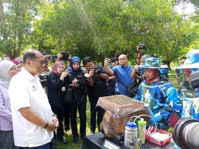 Mohamed Khaled (kiri) melihat demonstrasi cara pengambilan madu kelulut di bawah projek ekonomi MADANI di Kem Batu Tiga, Kluang.