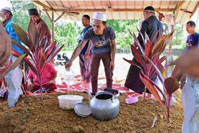 Azman menyiram air di pusara dua anaknya, Nur Shahila Shahirah Azman, 12, dan Nur Afiqah Shahirah Mohd Shawalluddin, 15, yang selamat dikebumikan dalam satu liang lahad di Tanah Perkuburan Islam Kampung Jeram, Manir, pada Rabu. Foto Bernama