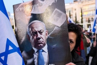 Penunjuk perasaan memegang plakad yang tertera slogan menuntut pengunduran Netanyahu. - Agensi