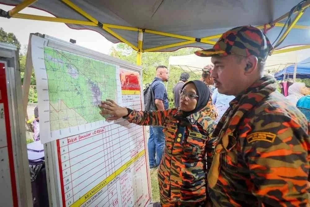 Pegawai Kanan Jabatan Bomba dan Penyelamat Malaysia (JBPM), Azliza Ahmad (kiri) melihat peta lokasi operasi mencari dan menyelamat (SAR) di Pos Kawalan Bomba di Bukit Changkat Asa di Tanjong Malim. Foto Bernama.