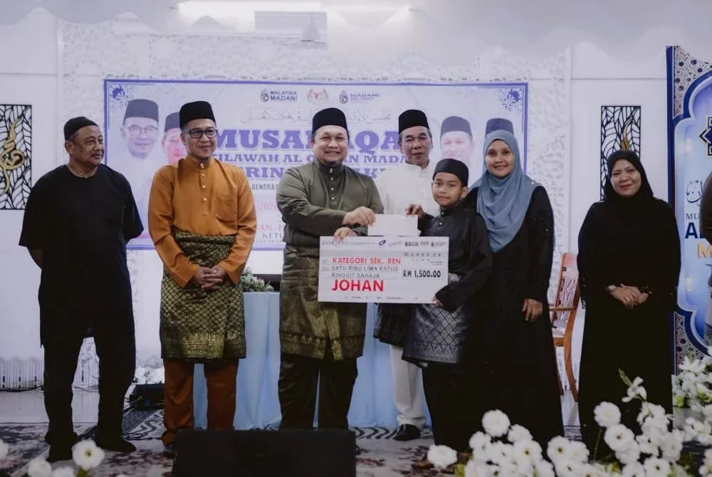 Ustaz Zamri menyampaikan hadiah kepada Nor Qalish Aqiff disaksikan oleh Pengerusi Komuniti MADANI Sri Aman, Pasir Puteh, Kamaruddin Mat Zin, dan Pengarah Jabatan Penerangan Negeri Kelantan, Muhd Nor Aswadi Md. Nor