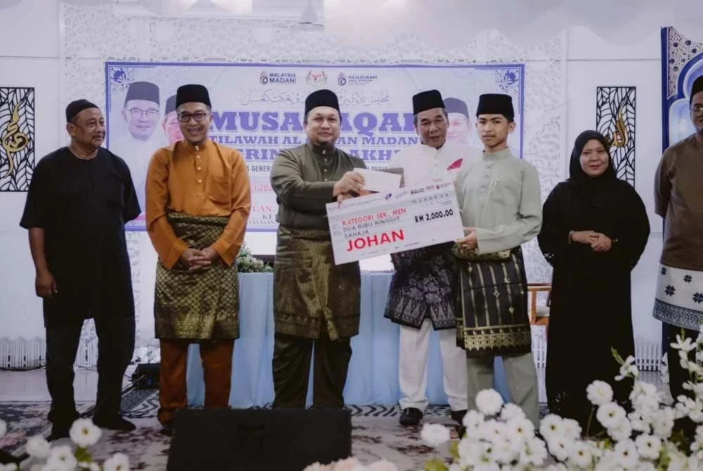 Ustaz Zamri menyampaikan hadiah kepada Muhamad Aduka Putra disaksikan oleh Pengerusi Komuniti MADANI Sri Aman, Pasir Puteh, Kamaruddin Mat Zin, dan Pengarah Jabatan Penerangan Negeri Kelantan, Muhd Nor Aswadi Md. Nor