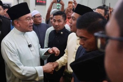 Anwar (kiri) menyantuni para jemaah selepas menunaikan Solat Jumaat di Masjid Meranti, Puchong. Foto Bernama