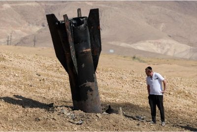 Seorang lelaki memeriksa sebuah roket yang terbenam di pinggir Jericho selepas Iran menggempur Israel pada Isnin. - Foto: AFP