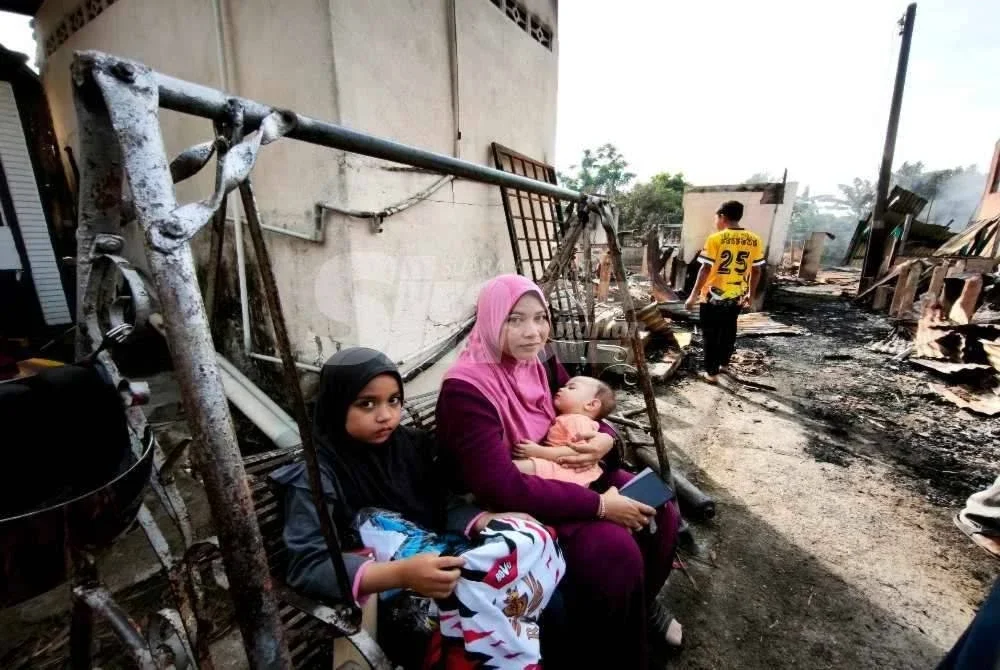 Eamie Zalina bersama anak-anaknya duduk di atas buaian yang merupakan satu-satunya harta benda peninggalan ibu bapanya yang berjaya diselamatkan dalam kebakaran di Kampung Cina, Gok Kapur, Kota Bharu pada Isnin. Foto: SINAR HARIAN/HAZELEN LIANA KAMARUDIN