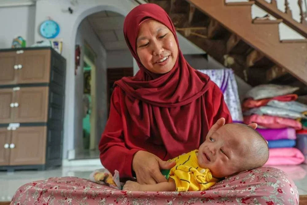 Siti Zakiah memangku Muhammad Rayqal yang kini seberat 2.9kg dan berusia empat bulan di rumahnya di Kampung Rhu 2, Marang. 