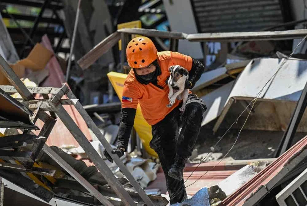 Seorang anggota penyelamat mendukung anjing pengesan ketika menjalankan operasi mencari dan menyelamat di sebuah bangunan runtuh susulan gempa bumi berukuran 7.8 magnitud di General Santos City pada 9 Jun 2026. Foto AFP