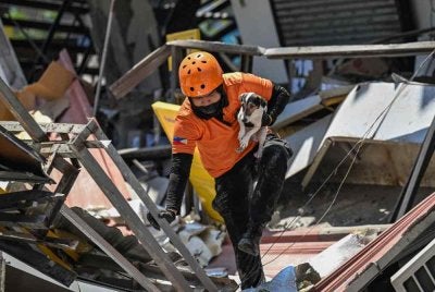 Seorang anggota penyelamat mendukung anjing pengesan ketika menjalankan operasi mencari dan menyelamat di sebuah bangunan runtuh susulan gempa bumi berukuran 7.8 magnitud di General Santos City pada 9 Jun 2026. Foto AFP