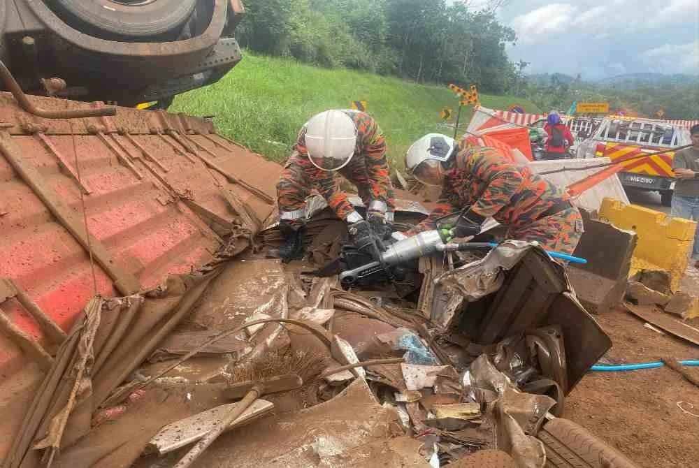 Anggota bomba dari BBP Bentong bertungkus-lumus membantu mengeluarkan mangsa yang tersepit dalam kereta di bawah treler yang terbalik. Foto JBPM Pahang