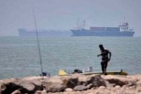 Seorang lelaki berdiri sambil memegang joran, ketika kapal kargo dan kapal komersial kelihatan di Selat Hormuz berhampiran Bandar Abbas, Iran, pada 17 Jun. Foto Gambar AP