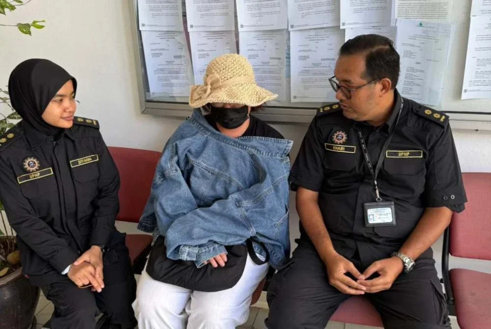 Tertuduh diiringi pegawai UPNP ketika dibawa ke Mahkamah Sesyen Raub pada Isnin bagi menghadapi tuduhan menduduki tanah kerajaan negeri secara haram kira-kira dua tahun lalu. Foto: UPNP
