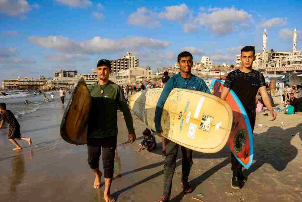 Mereka berjalan membawa papan luncur di pesisir Laut Mediterranean di Bandar, meneruskan rutin harian di sebalik ketegangan yang masih berlarutan. Foto: AFP