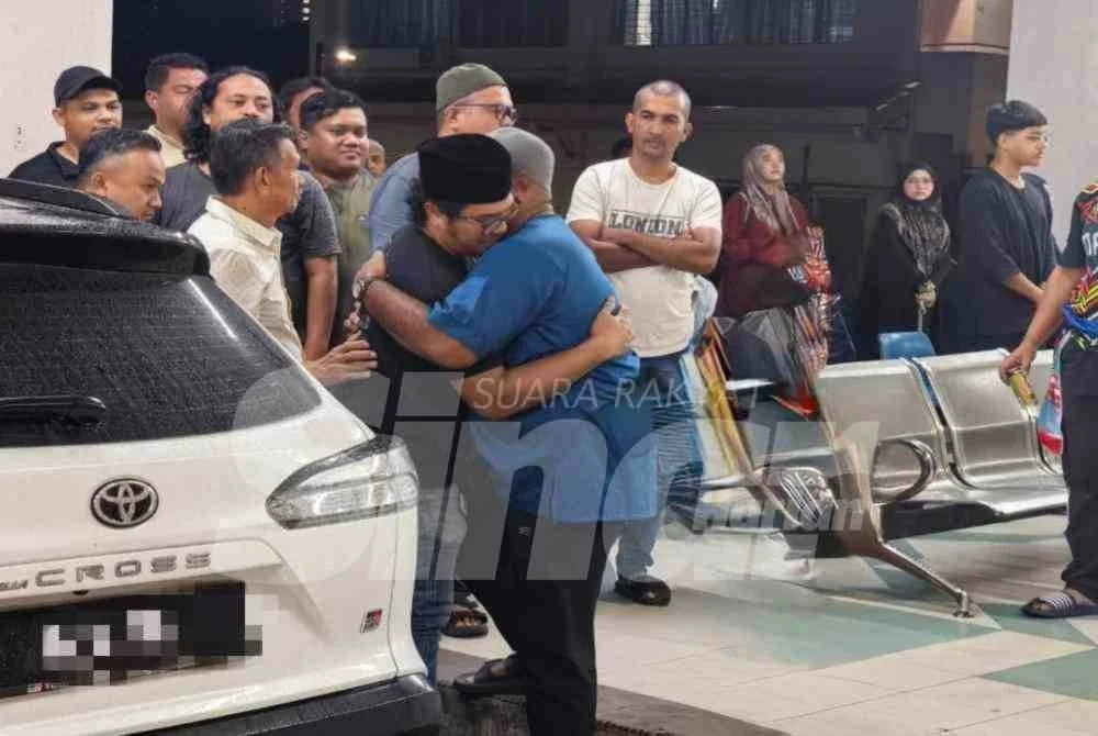 Mohd Aswandi (kiri) ditenangkan saudara mara dan kenalan yang hadir di Jabatan Forensik Melaka bagi proses menuntut jenazah anaknya yang meninggal dunia ketika latihan ragbi pada Rabu.