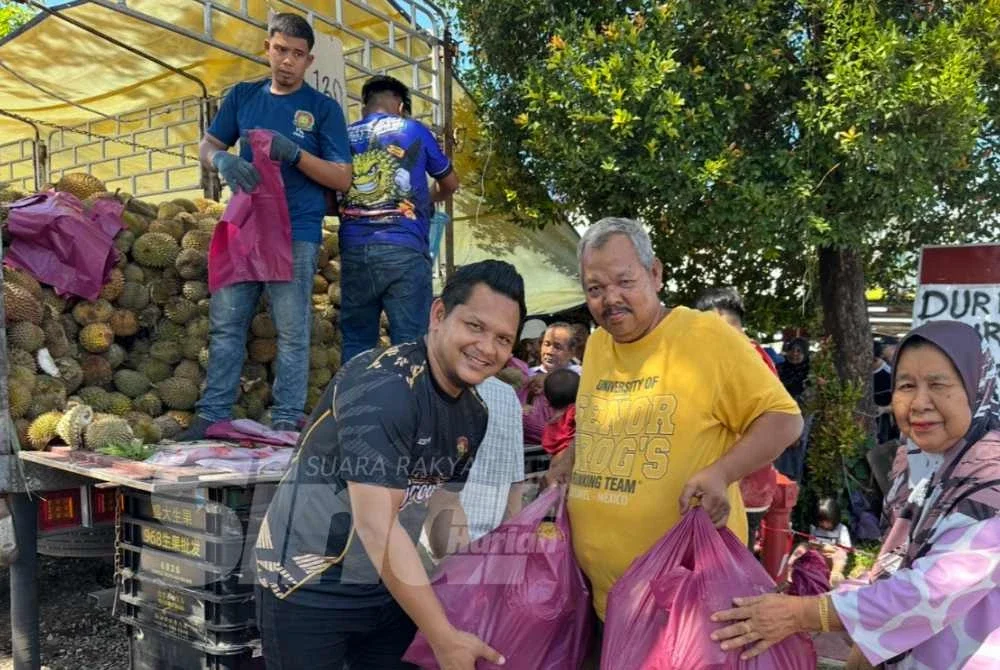 Shahmiazani (kiri) membantu mengangkat durian yang dibeli oleh pelanggan. - Foto SINAR HARIAN/ADILA SHARINNI WAHID
