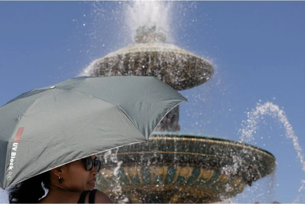 Seorang wanita berlindung daripada terik matahari menggunakan payung berhampiran sebuah air pancut di Dataran Place de la Concorde, Paris.