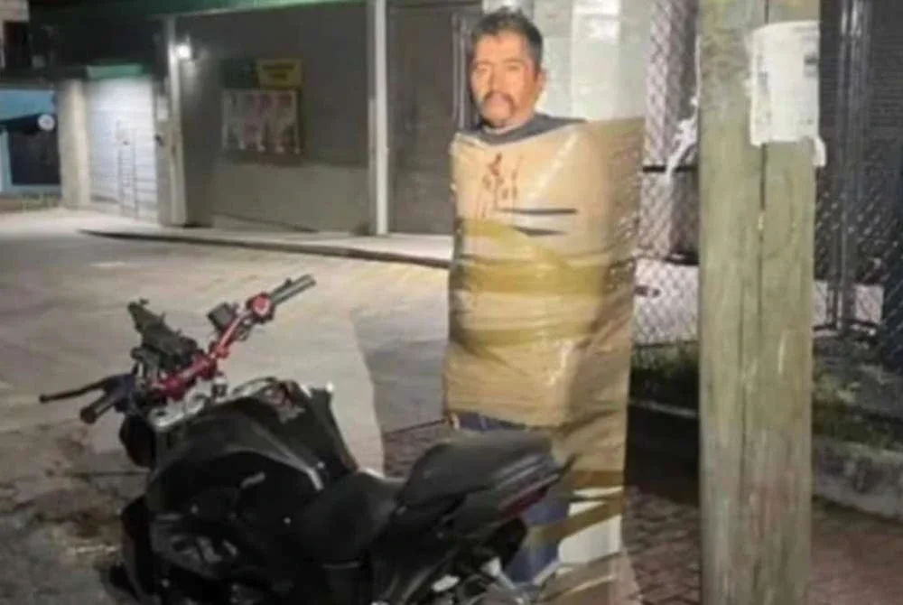 Seorang lelaki diikat pada sebatang tiang lampu bersama sebuah motosikal. Foto The Telegraph