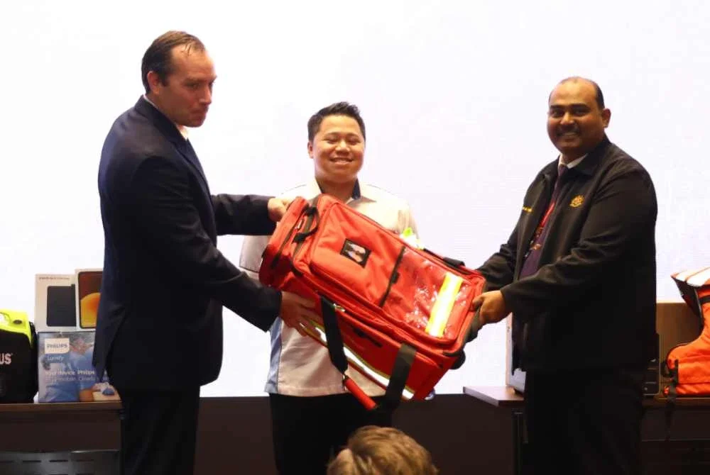 James (kiri) melakukan gimik penyerahan sumbangan peralatan perubatan kepada Dr Muthu Chelvan.