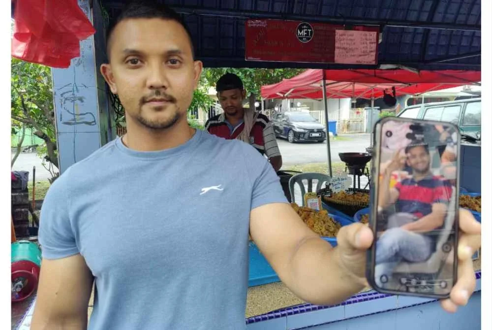 Shazni menunjukkan gambar arwah di hadapan gerai pisang goreng keluarganya di Seksyen 18 pada Rabu.