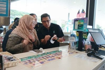 Fuziah (kiri) melihat resit pembayaran bantuan subsidi Budi Madani Diesel di Stesen Minyak Petronas Bandar Dato Onn pada Khamis.