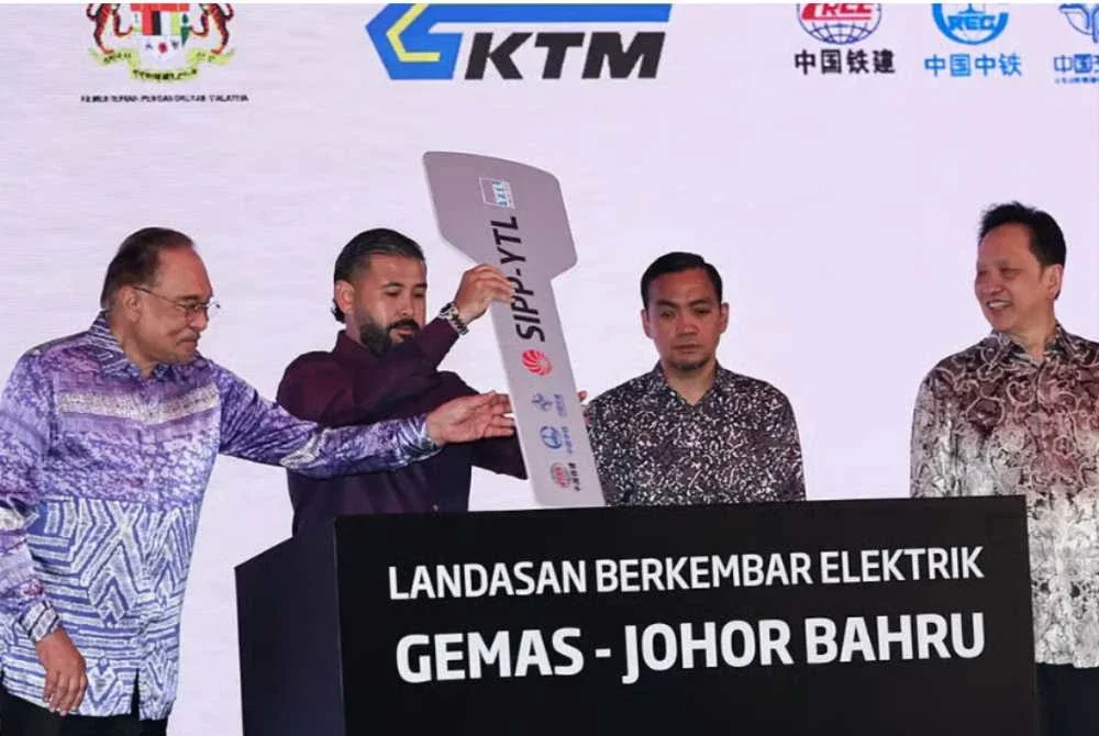 Tunku Mahkota Ismail (dua dari kiri) berkenan mencemar duli memasukkan replika kunci sebagai tanda simbolik penyerahan Landasan Berkembar Elektrik Gemas-Johor Bahru diiringi Anwar Ibrahim (kiri). - Foto: Bernama