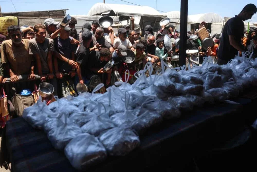 Penduduk Palestin menunggu giliran untuk mendapatkan masakan panas diagihkan dapur kendalian badan amal di Khan Yunis. Foto Agensi/AFP