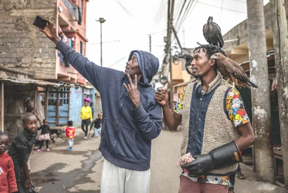 Seorang penduduk berswafoto bersama Magutha ketika dia membawa beberapa ekor burung yang dipeliharanya berjalan di luar. Foto AFP
