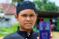 Muhammad Aqiff Amsyar menunjukkan gambar arwah bapanya semasa ditemui Kampung Bukit Merah, Paka pada Sabtu. Foto: Bernama 