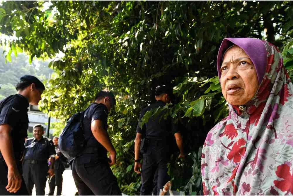 Ibu kepada mangsa, Salmah Shamsudin, 72, menunggu di lokasi kehilangan anaknya, Shahir Zainul, 45, sementara anggota polis memasuki kawasan semak ketika melancarkan operasi mencari dan menyelamat (SAR) bagi mengesannya selepas dilaporkan hilang sejak keluar dari rumahnya di Persiaran Mayang Pasir 2, Bayan Baru, dekat sini pada 10 Jun lepas. Foto Bernama. 