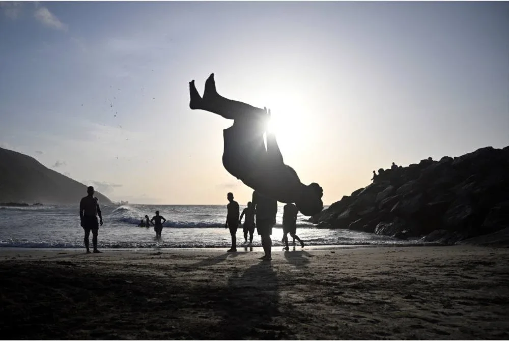 Beberapa pemuda menjalani aktiviti harian seperti biasa di tepi pantai berlatarbelakangkan pemandangan matahari terbenam. - Foto AFP