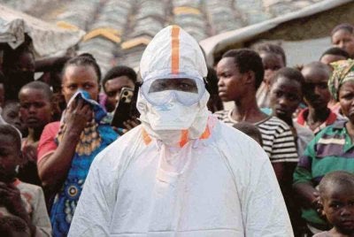 Seorang petugas kesihatan yang memakai peralatan pelindung diri berdiri berhampiran orang yang kehilangan tempat tinggal menunggu pengebumian mangsa yang disyaki Ebola, di Bunia, timur Republik Demokratik Congo, pada 18 Jun lalu. Foto/ Reuters