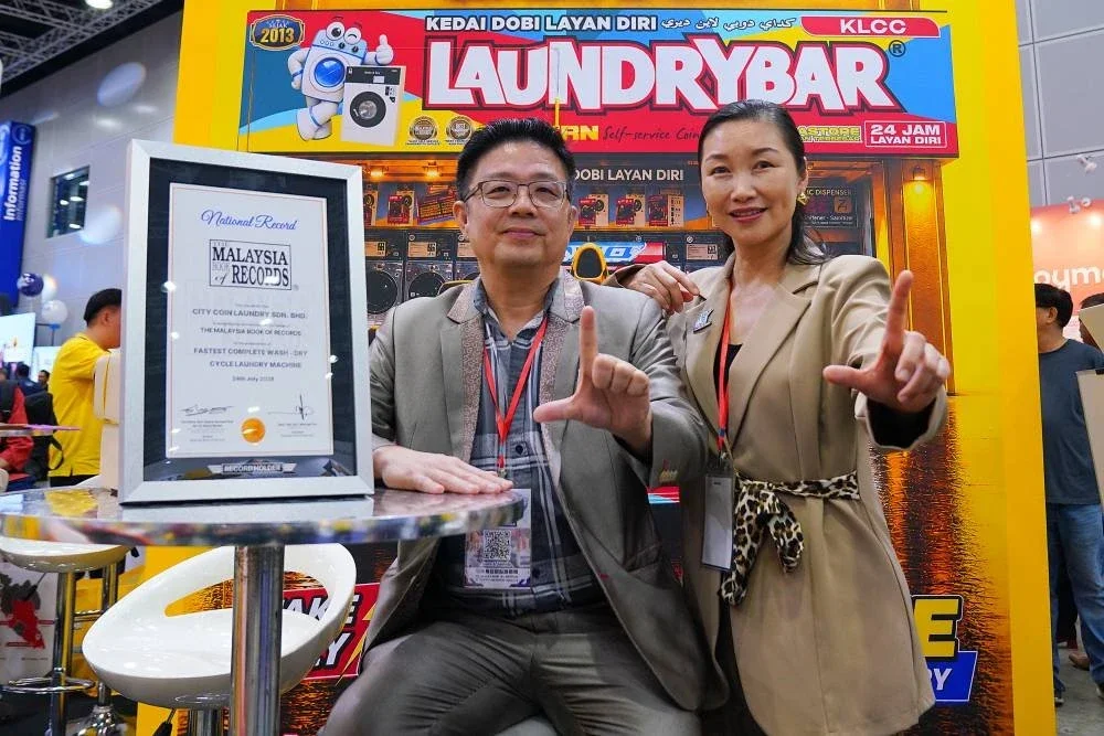 Paul Ang bersama Sandra Chua bergambar bersama sijil pengiktirafan Malaysia Book of Records yang diterima atas pencapaian menghasilkan mesin dobi layan diri kitaran basuh dan kering terpantas di Malaysia.