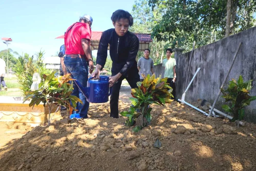 Muhamad Aiman Ashraf, 17, menyiram air di atas pusara ibu dan adiknya di Tanah Perkuburan Islam Kampung Melor Lama. Foto Bernama