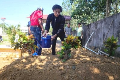 Muhamad Aiman Ashraf, 17, menyiram air di atas pusara ibu dan adiknya di Tanah Perkuburan Islam Kampung Melor Lama. Foto Bernama