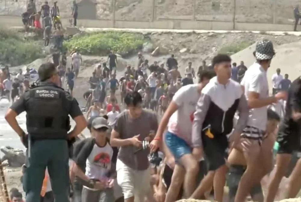 Migran berjalan melepasi anggota Pengawal Awam selepas berenang merentasi sempadan Ceuta dari Maghribi untuk memasuki wilayah Sepanyol, pada 30 Julai lalu. – Foto tular Reuters