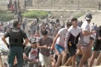 Migran berjalan melepasi anggota Pengawal Awam selepas berenang merentasi sempadan Ceuta dari Maghribi untuk memasuki wilayah Sepanyol, pada 30 Julai lalu. – Foto tular Reuters