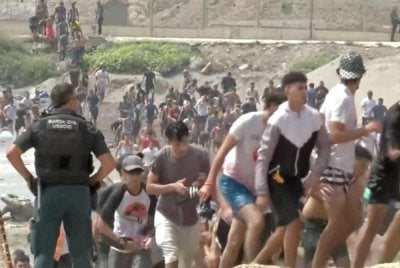 Migran berjalan melepasi anggota Pengawal Awam selepas berenang merentasi sempadan Ceuta dari Maghribi untuk memasuki wilayah Sepanyol, pada 30 Julai lalu. – Foto tular Reuters